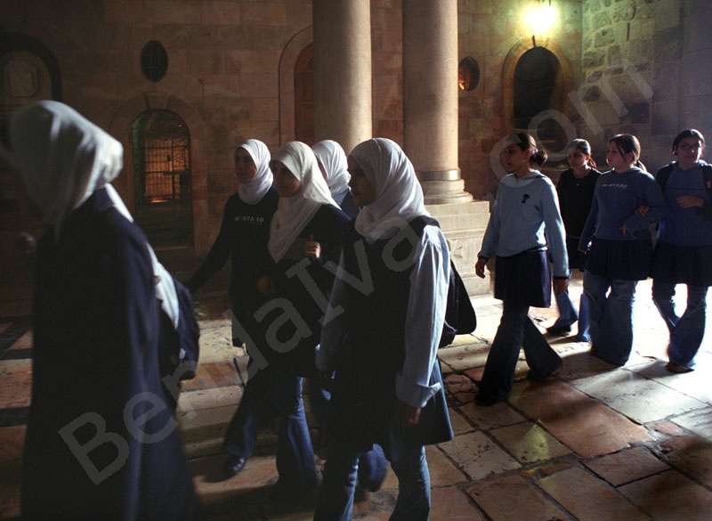     A templom előcsarnokában fejkendős arab keresztény iskolás lányok mennek Jézus sírjához. Mögöttük feljárat a Golgotához.   
