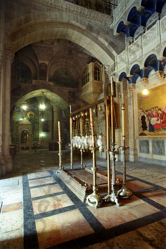 A Szentsír templom előcsarnokába beömlő napfényben a bebalzsamozás köve, felette a görög ortodox, a római katolikus, az örmény, a kopt, és Jakobita egyházak lámpása, háttér az örmény kápolna.