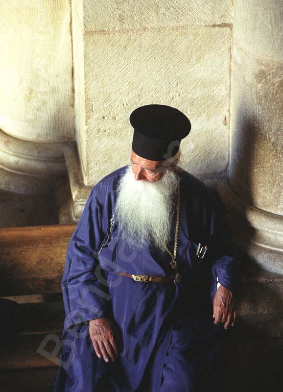 Jeruzsálem, keresztény negyed, szentsír templomban a bejárat melletti padon hosszú szakállas kék ruhában egy görög orthodox, ortodox pap. A beáradó fényben az ajtón kitekintve múlatja az időt.       