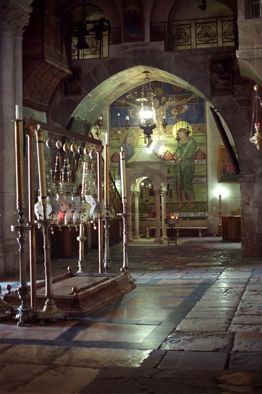 A bebalzsamozás kövét egy márványlap takarja el, fölötte lámpások vannak. Az előcsarnok kövezete legalább ezer éves. Hátérben a Három Mária kápolnában gyertya fénylik, A falon mozaik látható.         