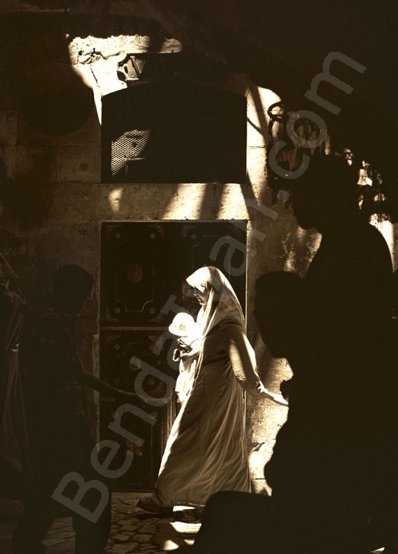   Arab nő gyerekekkel siet dolgára Jeruzsálem óvárosának arab negyedében. A sötét sikátorba beszűrődik a nyári nap sugara. A Via dolorosa, Jézus szenvedésének útja ma a legzajosabb része az arab negye