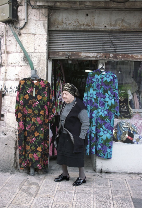         Idős ortodox zsidó nő áll egy ódon ruhás bolt előtt. Fején a hagyományos kendő. Mea Shearim ultraortodox negyedében gyakran látható az európai szemnek elavult mintájúnak tűnő ódivatú ruhákat.
