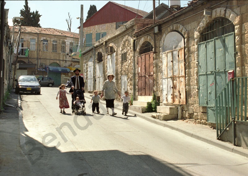      Ortodox zsidó család ünnepnapi sétája. Az apa tolja a gyerekkocsit, jobbján nagyobbacska leányka, a gyerekkocsiban a család legkisebb tagja, az anya jobb és bal kezén két apró legény vidáman lépk